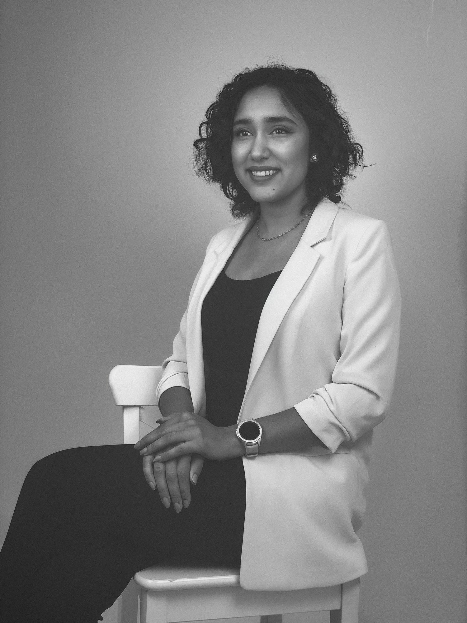 Black and white portrait of a woman sitting on a chair against a plain background