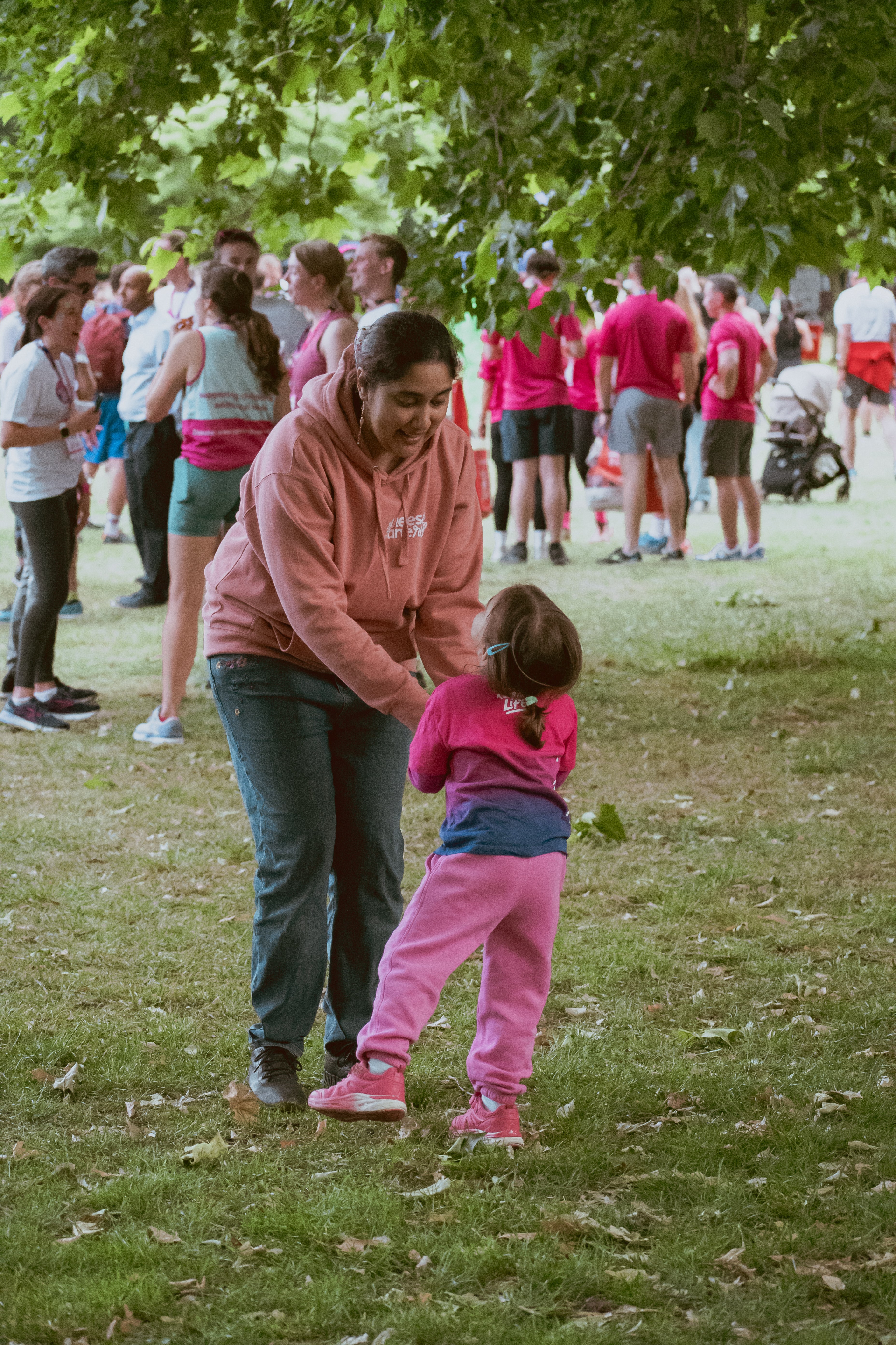 Woman and child in pink outfits interacting in a park with other people in the background